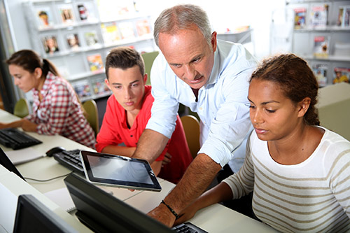 Man with younger people looking at computers in a library