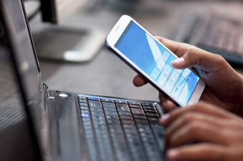 Image of a hand holding a mobile phone with their laptop